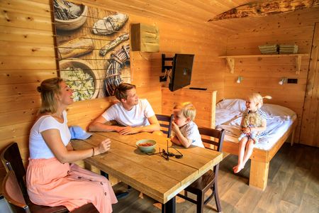 Familie am Esstisch im Germanenhaus klein, das Doppelbett im Hintergrund